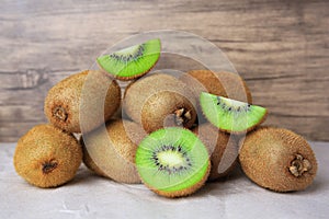 Heap of whole and cut fresh kiwis on parchment paper near wooden wall