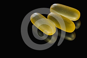 Heap of yellow capsule pills tablets medicine lying isolated on black background extreme close-up.