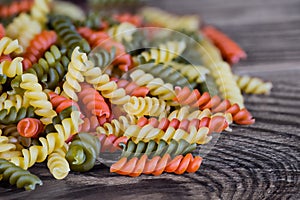 Heap of yellow, red and green fusilli pasta of helical shape on brown wooden background