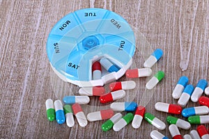 a Heaps of colorful capsules lie on a wooden table with a round pill dispenser for a week