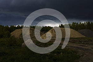 Heaps of sand at a construction site on city outskirts under storm clouds