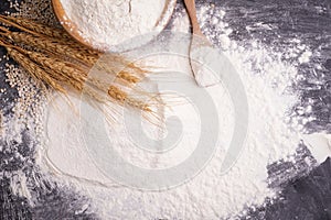 Heaps of wheat flour with ears of wheat on the table, black background - top view