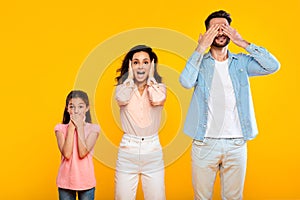 Hear no evil, see no evil, speak no evil. Family of three people covering eyes, ears and mouth, yellow background