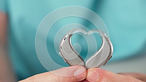 Hearing aids in hands making heart shape over blue background