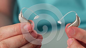 Hearing aids in hands making heart shape over blue background