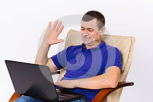 Hearing impaired. Disabled senior man sits in a leather armchair with a laptop smiling and waving. Online blog for deaf
