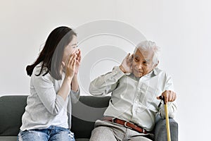 Hearing loss problem, Asian old man with hand on ear gesture trying to listen shouting woman. photo