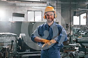 In hearing protection earphones. Factory worker in blue uniform is indoors