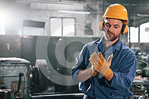 In hearing protection earphones. Factory worker in blue uniform is indoors