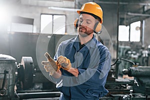 In hearing protection earphones. Factory worker in blue uniform is indoors