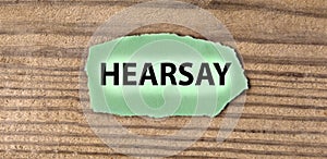HEARSAY - word on green torn piece of paper on old brown board background photo