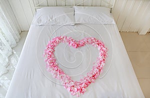 Heart of artificial pink rose petals on a bed. Honeymoon