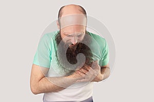 Heart attack or infarct. Portrait of sick middle aged bald bearded man in green t-shirt standing and holding his chest because