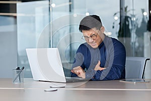 Heart attack at work. A young Asian man is sitting at a desk in the office, holding his heart