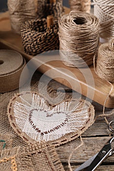 Heart of burlap fabric with stitches and spools of twine on wooden table