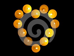 Heart with burning candles with a yellow flame on a black table with a blurred background. Christmas candles. Lighted candles at n