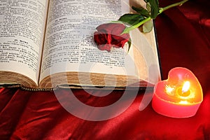 Heart candle on open Bible and red rose