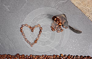 Heart from coffee beans with burlap and spoon at grey kitchen worktop background