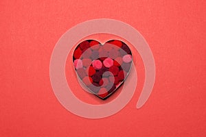 Heart cookie cutter full of terry fabric balls centred on red paper background. Valentines idea photo