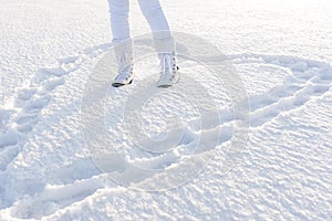 Heart in deep snow by footsteps. Concept of love. Woman legs dressed in warm winter boots.