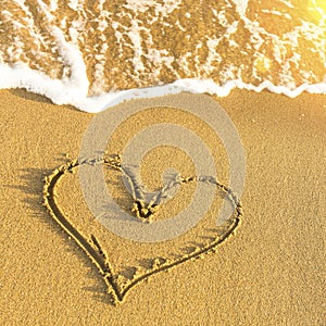 Heart drawn in beach sand, soft wave and solar glare. Love.