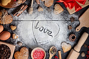 Heart drawn on flour with inscription Love. Gingerbread cookies, spices and baking supplies on black wood background