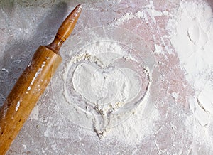 A heart is drawn on the flour scattered on the table, and a rolling pin for rolling out the dough lies next to it. The symbol of