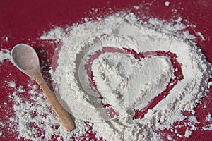 A heart drawn in a pile of flour next to a wooden spoon