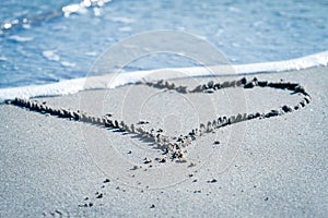 Heart drawn on the sand of the beach and blue sea waves with foam