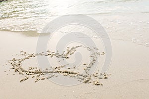 Heart drawn on a sand of beach with the wave of the sea in the bright sunlight.