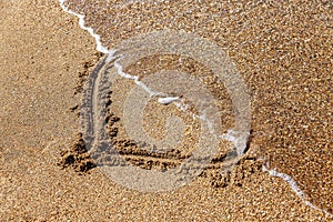 A heart drawn on the sand, half washed away by the wave. Love and relationship problems. Close-up