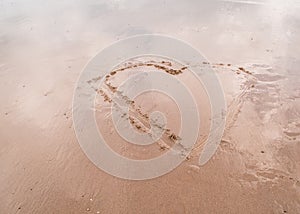 Heart drawn in the sand with sky reflected in wet sand