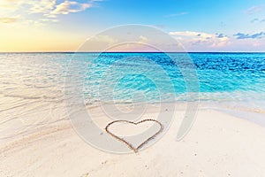 Heart drawn on sand of a tropical beach at sunset.