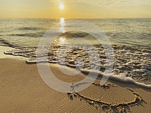 Heart drawn on a sandy beach by the ocean background of an incredibly beautiful sunset, sunrise. White foam of sea wave