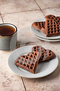 Heart form chocolate waffle cookies in white plate for Valentine's day with tea on pink tileba ckground. Sweet