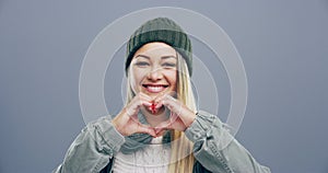 Heart, hands and face of woman with sign of love, kindness and donation in studio on grey background. Portrait of happy