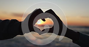 Heart hands, sunset and silhouette of a couple on the beach together for dating, romance or travel. Love, sky and nature