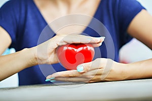 Heart health concept with womanâ€™s hands protecting a shiny red heart