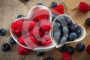 Heart healthy foods and good eating habits concept with two heart shaped white bowls of blueberries and raspberries with copy