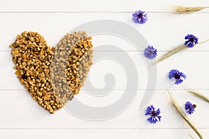 Heart laid out of granola, spikelets and cornflowers on white wooden background. Flat lay. Copy space