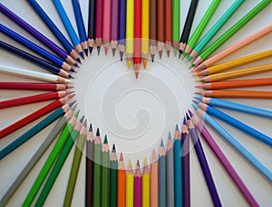 The heart is lined with bright colored wooden sharp pencils on white background