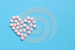 Heart lined with pink pills on a blue rubberized background, top view