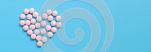 Heart lined with pink pills on a blue rubberized background, top view. Banner