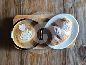 Heart love Latte art coffee in Black cup and Croissant topped with icing sugar