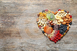 Heart made of different dried fruits and nuts on wooden background, top view.