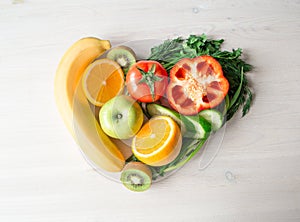 Heart made from different fruits and vegetables on light wooden table