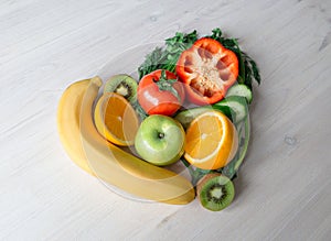 Heart made from different fruits and vegetables on light wooden table