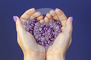 Heart made by hands from wax capsules for depilation. wax for depilation in lilac-colored capsules