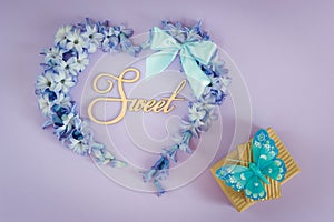 Heart made from hyacinth flowers with mint bow and gift boxes with butterfly on purple background.