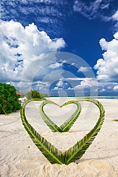 Heart made of palm tree leaves on tropical island with overwater bungalows in the background
